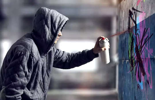 a young man wearing a hoodie spraying graffiti on a wall