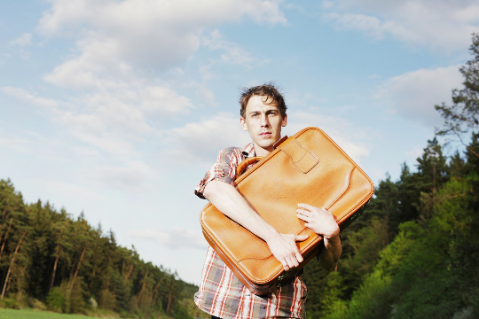 man standing outside clutching a suitcase to his chest