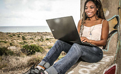 young woman sitting with her back against a tree working on her laptop