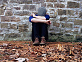 youth sitting alone outside with his head down on his arms